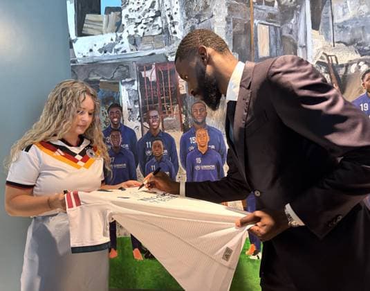 More than a football player: UNHCR Gamechanging Team Member Antonio Rudiger NEW YORK, UNITED STATES - JULY 23: Germany s Antonio Rudiger signs a Germany national team, Nationalteam jersey during an event with the UN Refugee Agency s (UNHCR) Gamechanging Team at the United Nations Headquarters in New York City, United States, on July 23, 2026. The symbolic team of global soccer players with refugee or displaced backgrounds joined UNHCR in calling for safety, protection, and opportunities for the world s 48.8 million displaced children. Selcuk Acar Anadolu New York United States. Editorial use only. Please get in touch for any other usage.  Copyright: x2026xAnadoluxSelcukxAcarx