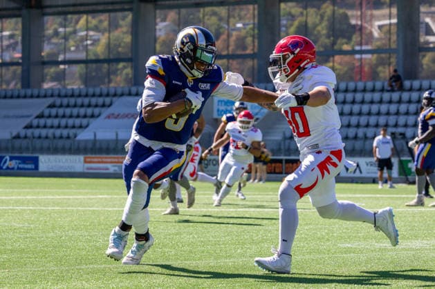 Alpine Rams tight end Jared Scott ( 5) drives forward using a stiff-arm against a Firenze Red Lions defender during a rushing play. Live game action captured on artificial turf with empty stadium seating in the background. Alpine Rams vs Firenze Red Lions, American Football, American Football League Europe, Week 12, 2026, 8.8.2026, Copyright: xPFA RicoxDoninellix