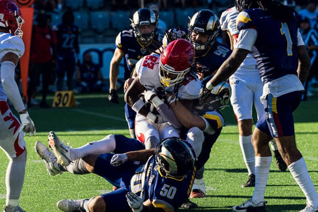 Alpine Rams defender Julien Ismael ( 50) tackles a Firenze Red Lions ball carrier Mali Harris-Strayhorn ( 83) on the ground alongside teammates to halt forward momentum during a rushing play in live game action. Firenze Red Lions player Thibaut Salvi ( 31) looks on from the field. The play occurs on artificial turf marked with yard lines in front of stadium seating. Alpine Rams vs Firenze Red Lions, American Football, American Football League Europe, Week 12, 2026, 8.8.2026, Copyright: xPFA RicoxDoninellix