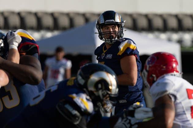 Alpine Rams quarterback Hank Bachmeier ( 8) scans the field from the pocket as offensive and defensive linemen engage at the line of scrimmage during play against the Firenze Red Lions. Bachmeier holds the football while searching for open receivers downfield. Unoccupied stadium seating and a sideline tent frame the background beyond the artificial turf. Alpine Rams vs Firenze Red Lions, American Football, American Football League Europe, Week 12, 2026, 8.8.2026, Copyright: xPFA RicoxDoninellix