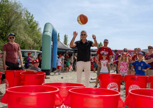 09.08.2026, Google Pixel Frauen-Bundesliga: Testspiel FC Bayern Frauen - Paris FC, im Sportpark Unterhaching, Fanfest vor dem Stadion, Präsident Herbert Hainer ( FC Bayern) macht einen Ballwurf in die Plastiktonnen bei den Basketballern am Stand *** August 9, 2026, Google Pixel Women s Bundesliga Friendly Match: FC Bayern Women vs. Paris FC, at Sportpark Unterhaching; fan festival in front of the stadium; FC Bayern President Herbert Hainer throws a ball into the plastic bins at the basketball team s booth