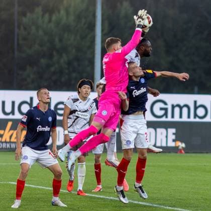Timon Weiner springt hoch und fängt den Ball sicher mit beiden Händen, während Ricky-Jade Jones vom FC St. Pauli und David Zec von KSV Holstein Kiel im Gedränge um ihn herum kämpfen. Mehrere Spieler beider Teams beobachten die Szene im Holstein-Stadion in Kiel. Ricky-Jade Jones und David Zec im Luftkampf beim Torwart-Abfangen *** Timon Weiner jumps high and catches the ball securely with both hands, while Ricky Jade Jones of FC St. Pauli and David Zec of KSV Holstein Kiel battle for it in the scramble around him. Several players from both teams watch the scene at Holstein Stadium in Kiel. Ricky Jade Jones and David Zec go head-to-head in the air as the goalkeeper makes the save. Copyright: xAndreasxTolksdorfx