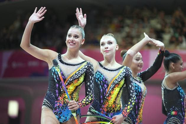 Drei Gymnastinnen eines Gruppenteams winken lächelnd dem Publikum in der Festhalle Frankfurt zu, während sie Keulen und Reifen in den Händen halten. Im Hintergrund ist eine vierte Athletin mit portugiesischer Flagge am Trikot zu sehen. Rhythmische Sportgymnastik WM 2026 – Gruppenteam winkt dem Publikum *** Three gymnasts from a group team smile and wave to the audience in Frankfurt’s Festhalle while holding clubs and hoops. In the background, a fourth athlete can be seen with a Portuguese flag on her leotard. 2026 Rhythmic Gymnastics World Championships – Group team waves to the audience Copyright: xspeedshotx