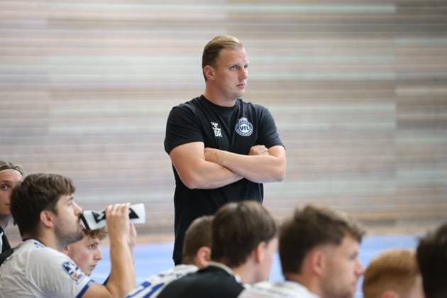 VfL Lübeck-Schwartau-Trainer David Röhrig steht mit verschränkten Armen konzentriert an der Seitenlinie und verfolgt das Spiel in der Hansehalle Lübeck. Im Hintergrund sitzen mehrere Spieler auf der Auswechselbank, darunter Guy Resch Ermann. David Röhrig beobachtet das Spielgeschehen von der Seitenlinie *** VfL Lübeck Schwartau coach David Röhrig stands on the sideline with his arms crossed, focused, watching the game at the Hansehalle in Lübeck. In the background, several players are sitting on the bench, including Guy Resch Ermann. David Röhrig watches the action from the sideline. Copyright: xspeedshotx