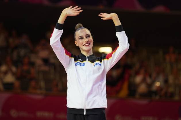 Eine Gymnastin im deutschen Nationaldress reckt strahlend lächelnd die Arme in die Höhe und feiert vor dem Publikum der Festhalle Frankfurt. Sie trägt die weiß-schwarz-rot-goldene Trainingsjacke des deutschen Teams mit den Sponsoren HYLO und SDK. Deutsche Gymnastin jubelt bei der Rhythmischen Sportgymnastik-WM in Frankfurt *** A gymnast in the German national uniform raises her arms high with a beaming smile and celebrates in front of the audience at the Festhalle in Frankfurt. She is wearing the German team’s white, black, red, and gold training jacket featuring the sponsors HYLO and SDK. A German gymnast cheers at the Rhythmic Gymnastics World Championships in Frankfurt. Copyright: xspeedshotx
