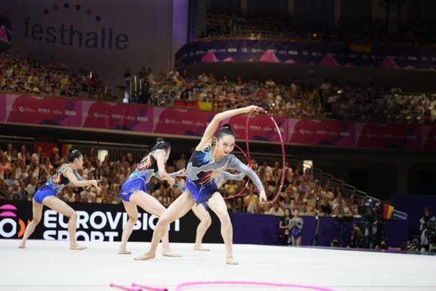 Drei Turnerinnen aus Team Japan führen in der Festhalle Frankfurt eine synchronisierte Gruppenübung mit Reifen und Stäben durch, während das Publikum die vollbesetzte Halle füllt. Im Vordergrund ist ein pinkes Seil auf dem Boden zu sehen, das auf ein weiteres Gerät der Übung hindeutet. Gruppenübung von Team Japan mit Reifen und Stäben bei der Rhythmischen Sportgymnastik-WM in Frankfurt *** Three gymnasts from Team Japan are performing a synchronized group routine with hoops and clubs at the Festhalle in Frankfurt, while the audience fills the packed hall. In the foreground, a pink rope can be seen on the floor, indicating another piece of equipment used in the routine. Team Japan’s group routine with hoops and clubs at the Rhythmic Gymnastics World Championships in Frankfurt Copyright: xspeedshotx