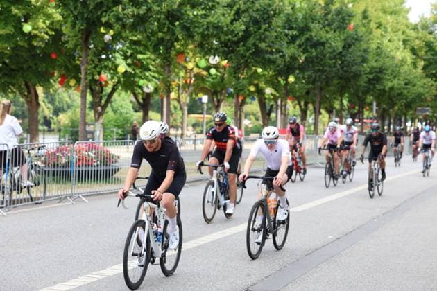 Eine Gruppe von Radsportlern fährt auf einer abgesperrten Straße in Hamburg, gesäumt von Bäumen und bunten Dekorationen. Im Vordergrund führt ein Fahrer in schwarzem Trikot und weißem Helm das Feld an. Radsportler im Peloton bei den Cyclassics Hamburg *** A group of cyclists rides down a closed-off street in Hamburg, lined with trees and colorful decorations. In the foreground, a rider in a black jersey and white helmet leads the pack of cyclists in the peloton at the Cyclassics Hamburg. Copyright: xspeedshotx xSarahxWolfx