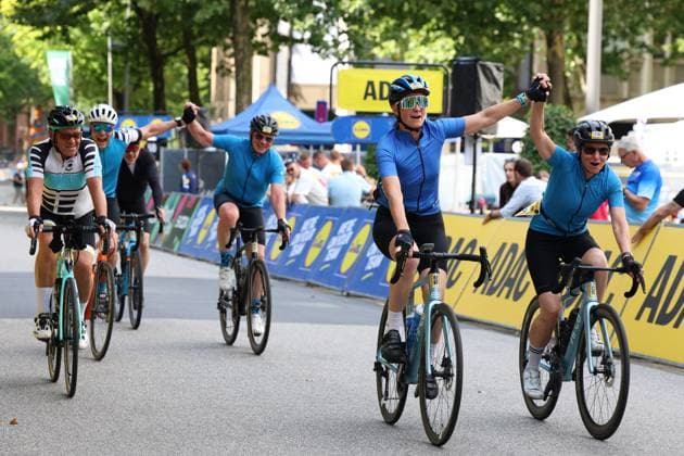 Mehrere Teilnehmer der Cyclassics Hamburg überqueren jubelnd die Ziellinie am Rathausmarkt, die Arme in die Höhe gestreckt. Im Hintergrund sind ADAC- und Lidl-Werbebanden sowie ein blaues Zelt sichtbar. Jubelnde Hobbyfahrer überqueren die Ziellinie bei den Cyclassics Hamburg *** Several participants in the Cyclassics Hamburg cross the finish line at Rathausmarkt, cheering and raising their arms in the air. In the background, ADAC and Lidl advertising banners and a blue tent are visible. Cheering amateur cyclists cross the finish line at the Cyclassics Hamburg. Copyright: xspeedshotx xSarahxWolfx