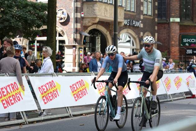 Zwei Radfahrer passieren die Dextro Energy-Absperrung am Rathausmarkt Hamburg beim Cyclassics-Rennen. Im Hintergrund verfolgen zahlreiche Zuschauer das Rennen vor historischer Kulisse. Zwei Radfahrer beim Cyclassics Hamburg am Rathausmarkt *** Two cyclists pass the Dextro Energy barrier at Hamburg s Rathausmarkt during the Cyclassics race. In the background, numerous spectators watch the race against a historic backdrop. Two cyclists at the Cyclassics Hamburg at Rathausmarkt Copyright: xspeedshotx xSarahxWolfx