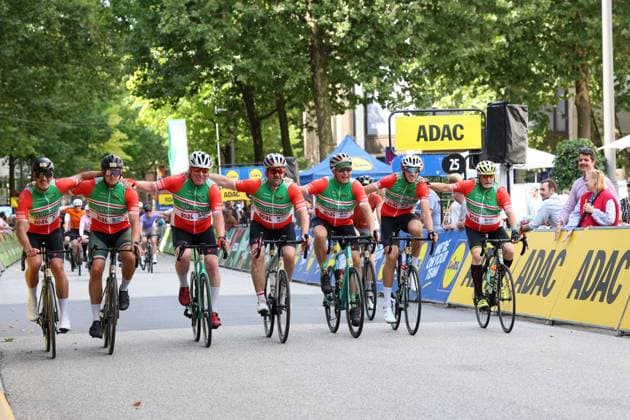 Eine Gruppe von Radfahrern in rot-grünen GlückStolz-Trikots überquert gemeinsam die Ziellinie der Cyclassics Hamburg am Rathausmarkt und feiert mit ausgebreiteten Armen. Im Hintergrund sind ADAC-Werbebanden und Zuschauer sichtbar. Jubelnde Gruppe beim Zieleinlauf der Cyclassics Hamburg am Rathausmarkt *** A group of cyclists wearing red-and-green GlückStolz jerseys crosses the finish line of the Cyclassics Hamburg at Rathausmarkt together and celebrates with arms outstretched. ADAC advertising banners and spectators are visible in the background. A cheering group at the finish of the Cyclassics Hamburg at Rathausmarkt Copyright: xspeedshotx xSarahxWolfx