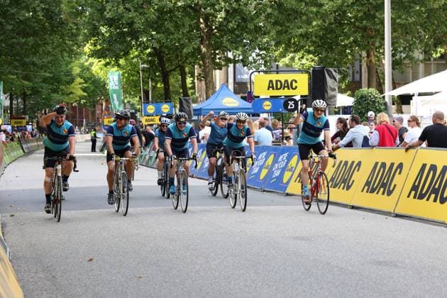 Eine Gruppe von Hobbyradfahrern in türkis-dunkelblauen Trikots überquert jubelnd die Ziellinie am Rathausmarkt Hamburg bei den Cyclassics. Mehrere Fahrer reißen die Arme in die Höhe, im Hintergrund sind ADAC- und Lidl-Werbebanden sowie Zuschauer zu sehen. Hobbyfahrer feiern Zieleinfahrt bei den Cyclassics Hamburg *** A group of amateur cyclists in turquoise and dark blue jerseys cross the finish line cheering at Hamburg’s Rathausmarkt during the Cyclassics. Several riders raise their arms in the air, with ADAC and Lidl advertising banners and spectators visible in the background. Amateur cyclists celebrate crossing the finish line at the Cyclassics in Hamburg Copyright: xspeedshotx xSarahxWolfx
