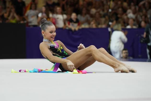 Sofiia Ilterikova sitzt lächelnd auf dem Wettkampfboden der Festhalle Frankfurt und hält die Endpose nach ihrer Kür mit bunten Bändern. Die farbenfrohen Bänder in Gelb, Pink, Blau und Lila liegen dekorativ um sie herum ausgebreitet. Sofiia Ilterikova bei Abschlusspose mit Bändern bei Rhythmischer Sportgymnastik WM *** Sofiia Ilterikova sits smiling on the competition floor of the Festhalle in Frankfurt, striking her final pose after her routine with colorful ribbons. The colorful ribbons in yellow, pink, blue, and purple are spread out decoratively around her. Sofiia Ilterikova strikes her final pose with ribbons at the Rhythmic Gymnastics World Championships Copyright: xspeedshotx