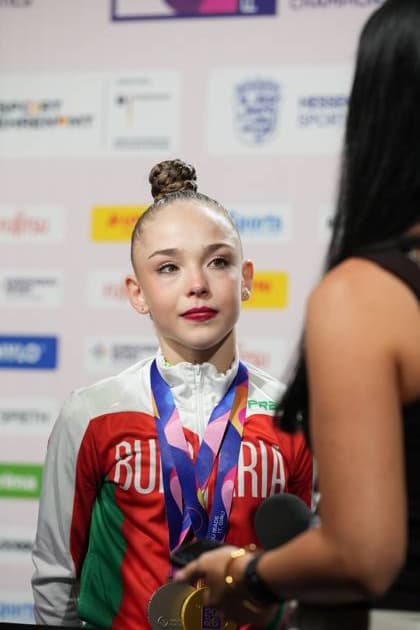 Eine Gymnastin aus Bulgarien steht mit mehreren Medaillen um den Hals vor einer Pressewall und gibt ein Interview. Im Hintergrund sind Sponsorenlogos der Weltmeisterschaft der rhythmischen Sportgymnastik 2026 in der Festhalle Frankfurt zu sehen. Bulgarische Gymnastin mit Goldmedaille beim Interview in Frankfurt *** A gymnast from Bulgaria stands in front of a press barrier with several medals around her neck, giving an interview. In the background are sponsor logos for the 2026 Rhythmic Gymnastics World Championships at the Festhalle in Frankfurt. Bulgarian gymnast with a gold medal during an interview in Frankfurt Copyright: xspeedshotx