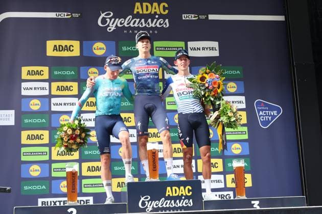 Paul Magnier ( 21; Soudal Quick-Step) steht auf dem obersten Podiumsplatz der ADAC Cyclassics Hamburg am Rathausmarkt, flankiert von Laurence Pithie ( 31; Red Bull – Bora – hansgrohe) auf Platz drei und einem weiteren Fahrer von Astana auf Platz zwei. Alle drei Fahrer halten Blumensträuße, auf dem Podium stehen Erdinger-Biergläser. Paul Magnier ( 21) gewinnt ADAC Cyclassics Hamburg – Siegerehrung auf dem Podium *** Paul Magnier 21 of Soudal Quick-Step stands on the top step of the podium at the ADAC Cyclassics Hamburg at Rathausmarkt, flanked by Laurence Pithie 31 of Red Bull – Bora – hansgrohe in third place and another Astana rider in second place. All three riders are holding bouquets of flowers; Erdinger beer glasses are on the podium. Paul Magnier (No. 21) wins the ADAC Cyclassics Hamburg – award ceremony on the podium Copyright: xspeedshotx xSarahxWolfx