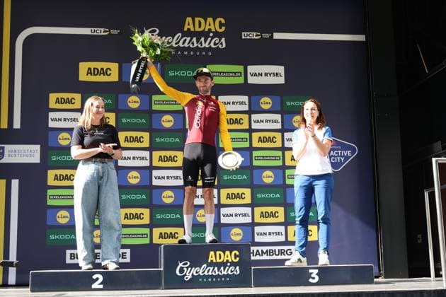Benjamin Thomas steht auf dem obersten Podiumsplatz der ADAC Cyclassics Hamburg und reckt den Siegerstrauß in die Höhe für den Gewinn der Bergwertung, in der anderen Hand hält er den Siegerpokal. Zwei Hostessen flankieren das Podium, während Sponsorenlogos von ADAC, Skoda, Lidl und Van Rysel den Hintergrund füllen. Benjamin Thomas ( 147) feiert Siegerehrung bei den ADAC Cyclassics Hamburg *** Benjamin Thomas stands on the top step of the podium at the ADAC Cyclassics Hamburg and raises the winner’s bouquet in celebration of his victory in the mountain classification; in his other hand, he holds the winner’s trophy. Two hostesses flank the podium, while sponsor logos from ADAC, Skoda, Lidl, and Van Rysel fill the background. Benjamin Thomas (147) celebrates at the awards ceremony for the ADAC Cyclassics Hamburg. Copyright: xspeedshotx xSarahxWolfx