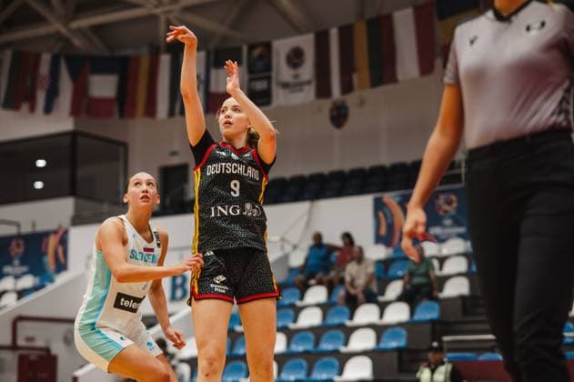 Ella Schrader ( 9; Team Deutschland u16w 2026) führt einen Wurfversuch aus, während eine Spielerin Sloweniens den Abpraller beobachtet. Im Hintergrund sind Länderflaggen und ein Schiedsrichter zu sehen. Ella Schrader ( 9; Deutschland u16w) beim Wurfversuch gegen Slowenien *** Ella Schrader 9 of Team Germany U16 Women 2026 attempts a shot while a Slovenian player watches the rebound. National flags and a referee can be seen in the background. Ella Schrader 9 of Team Germany U16 Women attempts a shot against Slovenia. Copyright: xJoelxKruehlerx