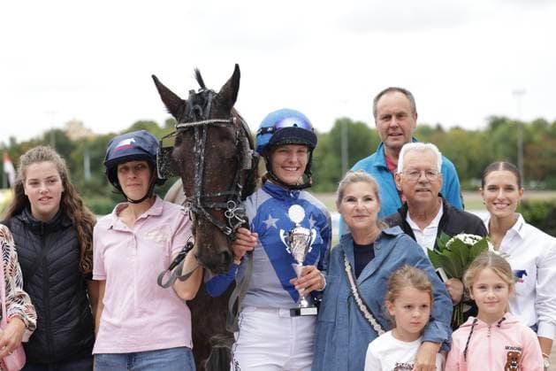 Eine Jockey in blauem Dress mit Helm hält einen Siegerpokal und posiert gemeinsam mit dem dunklen Rennpferd und mehreren Begleitpersonen für ein Gruppenfoto. Die Gruppe versammelt sich auf der Rennbahn Berlin Mariendorf zur Siegerehrung. Siegerfoto mit Jockey, Pferd und Begleitung nach dem Rennen *** A jockey in a blue outfit and helmet holds a winner s trophy and poses for a group photo alongside the dark-colored racehorse and several companions. The group gathers at the Berlin Mariendorf Racetrack for the award ceremony. A victory photo featuring the jockey, horse, and companions after the race. Copyright: xspeedshotx