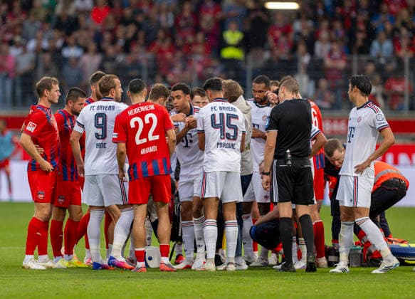 Sport Bilder des Tages #2 18.08.2026, Fussball Bundesliga 2026 2027, Testspiel, 1.FC Heidenheim - FC Bayern München, in der Voith-Arena Heidenheim, nach seinem erneuten Zusammenbruch während des Spieles, wird Jamal Musiala (mitte, Bayern München) vom Mannschaftsarzt Prof. Dr. Peter Ueblacker versorgt und danach vom Platz geführt. Spieler beider Mannschaften stehen besorgt um ihn herum. *** August 18, 2026, 2026–2027 Bundesliga, Friendly Match, 1. FC Heidenheim vs. FC Bayern Munich, at the Voith Arena in Heidenheim; after collapsing again during the game, Jamal Musiala (center), of Bayern Munich, is treated by team doctor Prof. Dr. Peter Ueblacker and then led off the field; players from both teams stand around him, concerned for his well-being