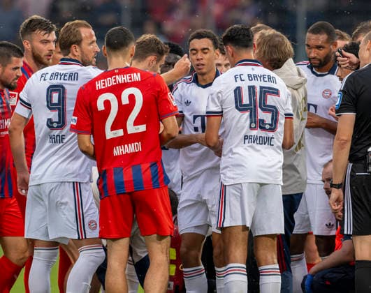 18.08.2026, Fussball Bundesliga 2026 2027, Testspiel, 1.FC Heidenheim - FC Bayern München, in der Voith-Arena Heidenheim, nach seinem erneuten Zusammenbruch während des Spieles, wird Jamal Musiala (mitte, Bayern München) vom Mannschaftsarzt Prof. Dr. Peter Ueblacker versorgt und danach vom Platz geführt. Spieler beider Mannschaften stehen besorgt um ihn herum. Harry Kane (li, FC Bayern München) streichelt ihm tröstend die Wange *** August 18, 2026, 2026–2027 Bundesliga, Friendly Match, 1. FC Heidenheim vs. FC Bayern Munich, at the Voith Arena in Heidenheim; after collapsing again during the game, Jamal Musiala (center), of Bayern Munich, is treated by team doctor Prof. Dr. Peter Ueblacker and then led off the field; players from both teams stand around him, concerned; Harry Kane (left), FC Bayern Munich, strokes his cheek comfortingly