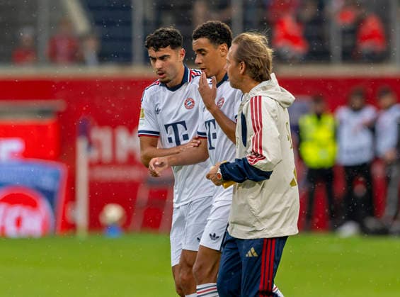 18.08.2026, Fussball Bundesliga 2026 2027, Testspiel, 1.FC Heidenheim - FC Bayern München, in der Voith-Arena Heidenheim, nach seinem erneuten Zusammenbruch während des Spieles, wird Jamal Musiala (mitte, Bayern München) vom Mannschaftsarzt Prof. Dr. Peter Ueblacker versorgt und vom Platz geführt. li: Aleksandar Pavlovic (Bayern München) nimmt ihn fürsorglich an die Hand *** August 18, 2026, 2026–2027 Bundesliga, Friendly Match, 1. FC Heidenheim vs. FC Bayern Munich, at the Voith Arena in Heidenheim. After collapsing again during the game, Jamal Musiala (center), of Bayern Munich, is treated by team doctor Prof. Dr. Peter Ueblacker and led off the field. Aleksandar Pavlovic of Bayern Munich takes him by the hand in a caring gesture.