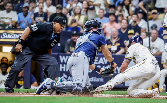 Home plate umpire Adrian Johnson watches as Milwaukee Brewers first baseman Jake Bauers (R) scores on Seattle Mariners catcher Cal Raleigh (C) in the first inning of the MLB, Baseball Herren, USA game between the Seattle Mariners and the Milwaukee Brewers at American Family Field in Milwaukee, Wisconsin on Tuesday, August 18, 2026.  MIL20260818808 TANNENxMAURY