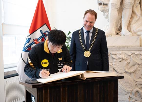 (260820) -- DUSSELDORF, Aug. 20, 2026 -- Fan Zhendong (L) signs on the Golden Book during the welcoming ceremony in Dusseldorf, Germany, Aug. 20, 2026. Chinese Table tennis, Tischtennis star Fan Zhendong was officially unveiled by his new club Borussia Dusseldorf at a press conference, PK, Pressekonferenz here on Thursday, as the Olympic champion prepares for his second season in the German Table Tennis Bundesliga and another campaign in European competition. ) (SP)GERMANY-DUSSELDORF-TABLE TENNIS-FAN ZHENDONG-CEREMONY ZhangxHaofu 