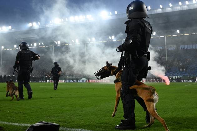 Mehrere Polizeibeamte in Schutzausrüstung und Helmen mit der Aufschrift MA betreten mit Diensthunden (Belgische Malinois mit Maulkorb) das Spielfeld des Carl-Benz-Stadions in Mannheim. Im Hintergrund sind Rauch und brennende Pyrotechnik aus dem Fanblock zu sehen. Polizeieinsatz mit Diensthunden auf dem Rasen im Carl-Benz-Stadion *** Several police officers in protective gear and helmets bearing the letters MA enter the field at the Carl Benz Stadium in Mannheim with police dogs—Belgian Malinois wearing muzzles. In the background, smoke and burning pyrotechnics can be seen coming from the fan section. Police operation with police dogs on the field at the Carl Benz Stadium Copyright: xMichaelxGelhardtx