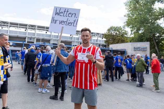 GER, Jena, Fussball, DFB-Pokal, 1. Hauptrunde, FC Carl-Zeiss Jena vs. SV Darmstadt 98 im Bild v.l.: Thomas Melchior , auf Social Media als Sportwettensheriff unterwegs, macht im Trikot des FC Rot-Weiss Erfurt und Spruchschild vor dem Stadion des FC Carl-Zeiss Jena auf Suchtpotenzial von Sportwetten aufmerksam , spricht mit Fans von Jena, geht in den Austausch 23.08.2026, Ernst Abbe Sportfeld Jena DFB REGULATIONS PROHIBIT ANY USE OF PHOTOGRAPHS AS IMAGE SEQUENCES AND OR QUASI-VIDEO, *** GER, Jena, Soccer, DFB Cup, First Round, FC Carl Zeiss Jena vs. SV Darmstadt 98: Pictured from left, Thomas Melchior, known on social media as the Sports Betting Sheriff, wearing an FC Rot Weiss Erfurt jersey and holding a sign in front of the FC Carl Zeiss Jena stadium to raise awareness about the addictive nature of sports betting, talking with Jena fans, engaging in conversation on August 23, 2026, Ernst Abbe Sportfeld, Jena. DFB REGULATIONS PROHIBIT ANY USE OF PHOTOGRAPHS AS IMAGE SEQUENCES AND OR QUASI-VIDEO, Copyright: HMBxMedia PaulxFritz