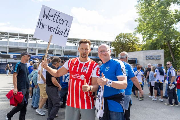 GER, Jena, Fussball, DFB-Pokal, 1. Hauptrunde, FC Carl-Zeiss Jena vs. SV Darmstadt 98 im Bild v.l.: Thomas Melchior , auf Social Media als Sportwettensheriff unterwegs, macht im Trikot des FC Rot-Weiss Erfurt und Spruchschild vor dem Stadion des FC Carl-Zeiss Jena auf Suchtpotenzial von Sportwetten aufmerksam , spricht mit Fans von Jena, geht in den Austausch 23.08.2026, Ernst Abbe Sportfeld Jena DFB REGULATIONS PROHIBIT ANY USE OF PHOTOGRAPHS AS IMAGE SEQUENCES AND OR QUASI-VIDEO, *** GER, Jena, Soccer, DFB Cup, First Round, FC Carl Zeiss Jena vs. SV Darmstadt 98: Pictured from left, Thomas Melchior, known on social media as the Sports Betting Sheriff, wearing an FC Rot Weiss Erfurt jersey and holding a sign in front of the FC Carl Zeiss Jena stadium to raise awareness about the addictive nature of sports betting, talking with Jena fans, engaging in conversation on August 23, 2026, Ernst Abbe Sportfeld, Jena. DFB REGULATIONS PROHIBIT ANY USE OF PHOTOGRAPHS AS IMAGE SEQUENCES AND OR QUASI-VIDEO, Copyright: HMBxMedia PaulxFritz