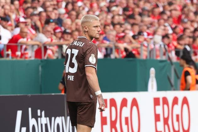Louis Oppie vom FC St. Pauli steht auf dem Spielfeld im Stadion an der Hafenstraße in Essen und blickt über die Schulter. Im Hintergrund sind die rot-weißen Fans von Rot-Weiss Essen auf der Tribüne zu sehen. Louis Oppie (FC St. Pauli) im Spiel gegen Rot-Weiss Essen *** Louis Oppie of FC St. Pauli is standing on the field at the stadium on Hafenstraße in Essen and looking over his shoulder. In the background, the red-and-white fans of Rot-Weiss Essen can be seen in the stands. Louis Oppie of FC St. Pauli in the game against Rot-Weiss Essen Copyright: xRuhr.Pottraitx