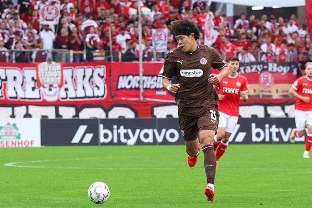 Ein Spieler des FC St. Pauli läuft mit dem Ball am Fuß über den Rasen, verfolgt von einem Spieler von Rot-Weiss Essen. Im Hintergrund ist die vollbesetzte Tribüne mit rot-weißen Fanblöcken zu sehen. FC St. Pauli ( 13) dribbelt am Ball im Stadion an der Hafenstraße *** An FC St. Pauli player runs across the field with the ball at his feet, followed by a Rot Weiss Essen player. In the background, the packed stands are filled with red-and-white fan sections. FC St. Pauli No. 13 dribbles the ball in the stadium on Hafenstraße. Copyright: xRuhr.Pottraitx
