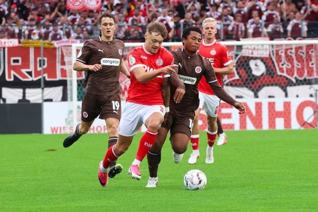Jannik Hofmann von Rot-Weiss Essen behauptet den Ball im intensiven Zweikampf gegen Joel Chima Fujita und Martijn Kaars vom FC St. Pauli. Im Hintergrund verfolgt Janne Sietan ( 22; Rot-Weiss Essen) die Szene im Stadion an der Hafenstraße. Jannik Hofmann im Zweikampf gegen Joel Chima Fujita und Martijn Kaars *** Jannik Hofmann of Rot Weiss Essen holds onto the ball in a fierce duel against Joel Chima Fujita and Martijn Kaars of FC St. Pauli. In the background, Janne Sietan (No. 22, Rot Weiss Essen) watches the action at the Hafenstraße Stadium. Jannik Hofmann in a duel against Joel Chima Fujita and Martijn Kaars Copyright: xRuhr.Pottraitx