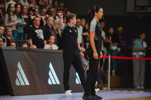 Ein Trainer in schwarzem Outfit gibt mit erhobenem Zeigefinger eine taktische Anweisung an der Seitenlinie der Sparkassen-Arena in Göttingen. Neben ihm steht eine große Spielerin in schwarzem Outfit, im Hintergrund sind zahlreiche Zuschauer zu sehen. Bundestrainerin und Spielerin an der Seitenlinie beim Deutschland-Spiel *** A coach in a black uniform gives a tactical instruction with his index finger raised on the sideline of the Sparkassen Arena in Göttingen. Standing next to him is a tall player in a black uniform; numerous spectators can be seen in the background. The national team coach and a player on the sideline during the Germany game Copyright: xJoelxKruehlerx
