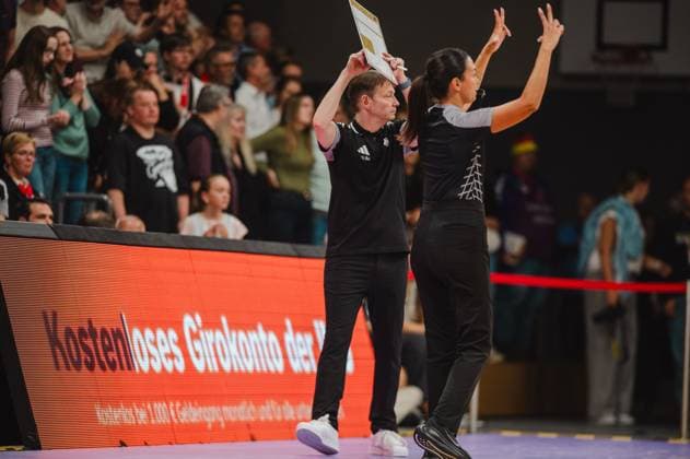 An der Seitenlinie der Sparkassen-Arena Göttingen hält ein Trainer ein Klemmbrett hoch, während eine Spielerin mit erhobenen Armen gestikuliert. Im Hintergrund verfolgen zahlreiche Zuschauer das Geschehen. Trainer und Spielerin an der Seitenlinie beim Basketball-Länderspiel *** On the sidelines of the Sparkassen Arena in Göttingen, a coach holds up a clipboard while a player gestures with her arms raised. In the background, numerous spectators watch the action. Coach and player on the sidelines during an international basketball game. Copyright: xJoelxKruehlerx