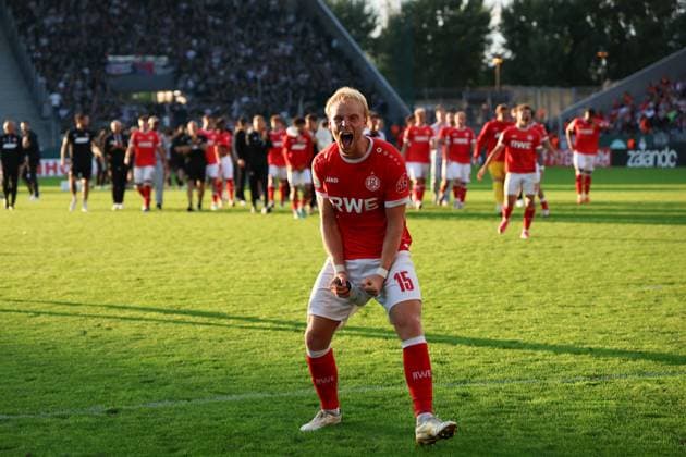 Ben Hüning ( 15; Rot-Weiss Essen) reißt die Fäuste nach unten und schreit seinen Jubel heraus, während die gesamte Mannschaft hinter ihm auf den Rasen des Stadions an der Hafenstraße strömt. Im Hintergrund sind auch Spieler des Gegners sowie eine vollbesetzte Tribüne zu sehen. Ben Hüning ( 15; Rot-Weiss Essen) jubelt ausgelassen nach dem Sieg *** Ben Hüning, No. 15 of Rot Weiss Essen, pumps his fists and lets out a shout of joy, while the entire team behind him floods onto the field at the stadium on Hafenstraße. In the background, players from the opposing team and a packed grandstand can be seen. Ben Hüning, No. 15 for Rot-Weiss Essen, celebrates exuberantly after the victory. Copyright: xRuhr.Pottraitx