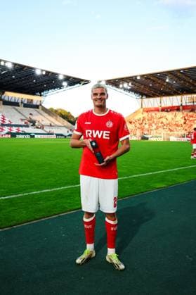 Marek Janssen ( 20; Rot-Weiss Essen) steht lächelnd auf dem Rasen des Stadions an der Hafenstraße und hält eine Trophäe in den Händen. Im Hintergrund sind Teile der Tribüne mit Zuschauern sowie das Spielfeld zu sehen. Marek Janssen ( 20; Rot-Weiss Essen) mit Auszeichnung im Stadion an der Hafenstraße *** Marek Janssen 20 of Rot-Weiss Essen stands smiling on the field at the stadium on Hafenstraße, holding a trophy in his hands. In the background, parts of the stands filled with spectators and the playing field can be seen. Marek Janssen 20 of Rot-Weiss Essen receives an award at the stadium on Hafenstraße. Copyright: xRuhr.Pottraitx