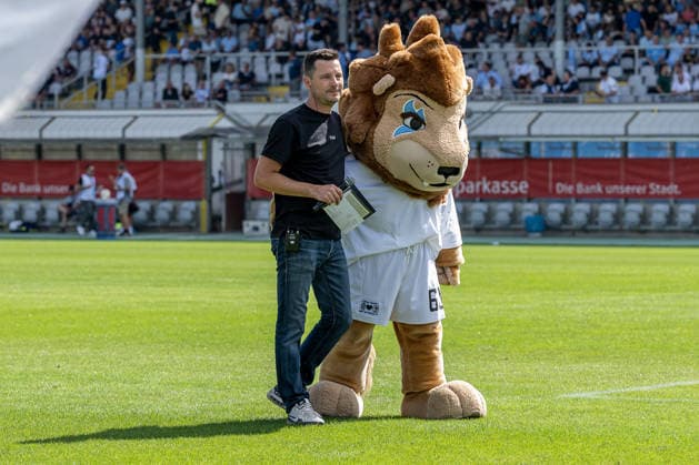 Sebastian Schaech (Stadionsprecher, TSV 1860 Muenchen) und Maskottchen Sechzgerl (TSV 1860 Muenchen) auf dem Rasen vor der Fankurve GER, TSV 1860 Muenchen vs. TSV Landsberg 1882, Fussball, Regionalliga Bayern, 6. Spieltag, Saison 2026 2027, 30.08.2026. (DFL DFB REGULATIONS PROHIBIT ANY USE OF PHOTOGRAPHS as IMAGE SEQUENCES and or QUASI-VIDEO). Foto: HMB Media Heike Feiner Copyright: HMBxMedia HeikexFeiner
