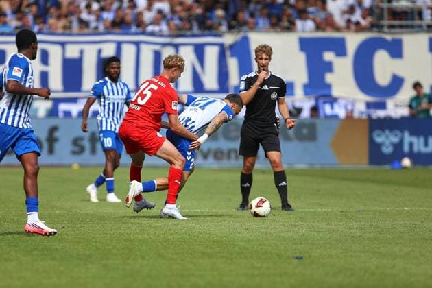 Magdeburg, Sachsen-Anhalt, Deutschland, 30.08.2026: Avnet Arena: 3. Spieltag, Saison 2026 27, 2. Fußball-Bundesliga: 1. FC Magdeburg - Holstein Kiel: Kasper Davidsen (15, Holstein Kiel) und Falko Michel (21, 1. FC Magdeburg) vor den strengen Augen von Schiedsrichter Jarno Wienefeld *** Magdeburg, Saxony-Anhalt, Germany, August 30, 2026, Avnet Arena, Matchday 3, 2026–27 Season, 2. Bundesliga, 1. FC Magdeburg vs. Holstein Kiel, Kasper Davidsen (15), Holstein Kiel, and Falko Michel (21), 1. FC Magdeburg, under the watchful eye of referee Jarno Wienefeld Copyright: xdtsxNachrichtenagenturx dts_131755