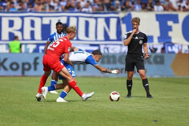 Magdeburg, Sachsen-Anhalt, Deutschland, 30.08.2026: Avnet Arena: 3. Spieltag, Saison 2026 27, 2. Fußball-Bundesliga: 1. FC Magdeburg - Holstein Kiel: Kasper Davidsen (15, Holstein Kiel) und Falko Michel (21, 1. FC Magdeburg) vor den strengen Augen von Schiedsrichter Jarno Wienefeld *** Magdeburg, Saxony-Anhalt, Germany, August 30, 2026, Avnet Arena, Matchday 3, 2026–27 Season, 2. Bundesliga, 1. FC Magdeburg vs. Holstein Kiel, Kasper Davidsen (15), Holstein Kiel, and Falko Michel (21), 1. FC Magdeburg under the watchful eye of referee Jarno Wienefeld Copyright: xdtsxNachrichtenagenturx dts_131762