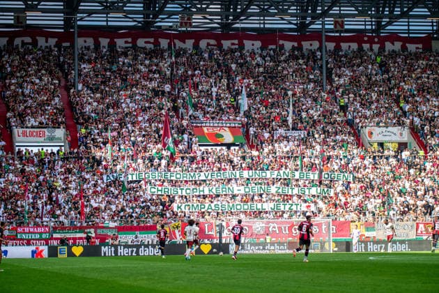 FC Augsburg Fans mit dem Banner Aufstiegsreform? Vereine uns Fans betrogen! Chrisoph Kern- Deine Zeit ist um! Kompassmodell jetzt! beim Bundesligaspiel FC Augsburg - Bayer 04 Leverkusen am 12.09.2026. Augsburg WWK Arena Bayern Deutschland *** FC Augsburg fans holding a banner reading: Promotion Reform: Clubs and Fans Have Been Betrayed Christoph Kern, Your Time Is Up Compass Model at the Bundesliga match between FC Augsburg and Bayer 04 Leverkusen on September 12, 2026, at the WWK Arena in Augsburg, Bavaria, Germany