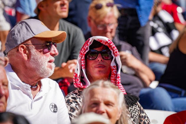 Deutschland: Fussball Bundesliga 2026 - 2027, 3. Spieltag - SC Freiburg vs Borussia Mönchengladbach - Europa-Park-Stadion (Freiburg): Zuschauer und Fans des SC Freiburg auf der Tribüne bei sonnigem Wetter. Frau schützt sich mit einem rot-weißen Fanschal über dem Kopf vor starker Sonneneinstrahlung und Hitze. Sommer, Sonne, Hitze, Sonnenschutz, Hitzeschutz, hohe Temperaturen, Fußballfan, Fans, Zuschauer, Tribüne, SC Freiburg, Stadion. *** Germany Soccer Bundesliga 2026–2027, Matchday 3: SC Freiburg vs. Borussia Mönchengladbach at Europa-Park Stadium in Freiburg; spectators and SC Freiburg fans in the stands on a sunny day; a woman shields herself from the strong sunlight and heat with a red-and-white fan scarf draped over her head; summer, sun, heat, sun protection, heat protection, high temperatures, soccer fan, fans, spectators, stands, SC Freiburg, stadium Copyright: xJOERANxSTEINSIEKx