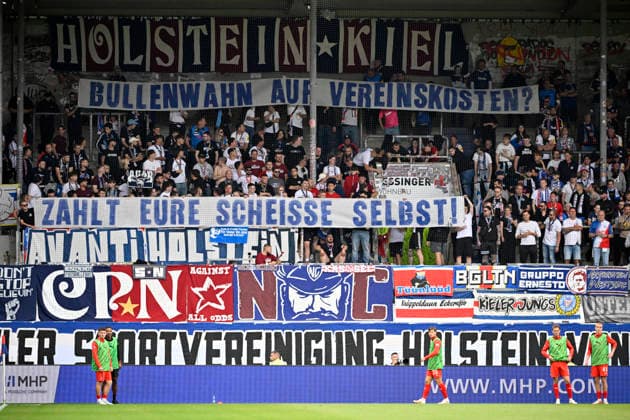 Fanblock, Fans, Fankurve, Flaggen, Fahnen, Stimmung, stimmungsvoll Transparent, Protest, Protestplakat, Fanplakat, Banner, Plakat, Spruchband gegen Kostenverteilung bei Polizeieinsatz 1. FC Heidenheim 1846 FCH vs Holstein Kiel KSV 13.09.2026 DFL REGULATIONS PROHIBIT ANY USE OF PHOTOGRAPHS AS IMAGE SEQUENCES AND OR QUASI-VIDEO 1. FC Heidenheim 1846 FCH vs Holstein Kiel KSV