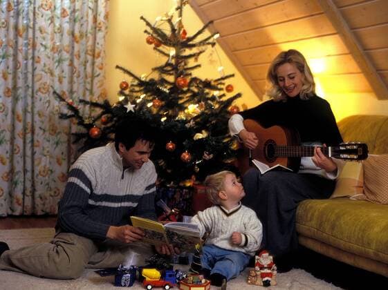 Vater , Mutter und Kind bei der Bescherung am Heiligabend , die Mutter stimmt ein Liedchen auf der Gitarre an