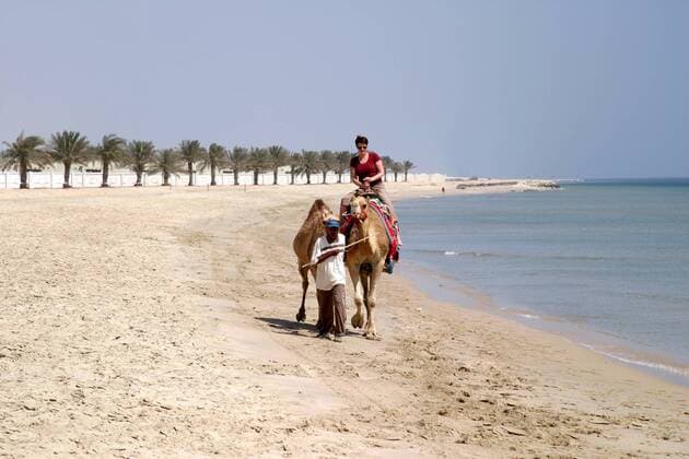 Touristin reitet auf einem Kamel am Strand der Sealine Beach Resort bei Mesaieed - Katar
