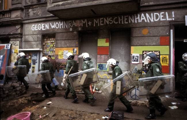 Polizisten laufen vor einer Hauswand mit dem Schriftzug - Gegen Wohnraum und Menschenhandel - während der Räumung besetzter Hauser in der Mainzer Straße in Berlin-Friedrichshain