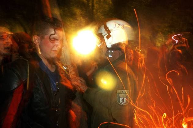 Jugendlicher und Polizist neben einem Feuer während Krawallen in der Walpurgisnacht am Boxhagener Platz in Berlin-Friedrichshain