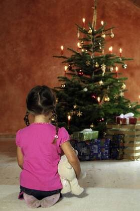 Bescherung - Kleines Mädchen kniet mit Teddy einsam vor dem Weihnachtsbaum