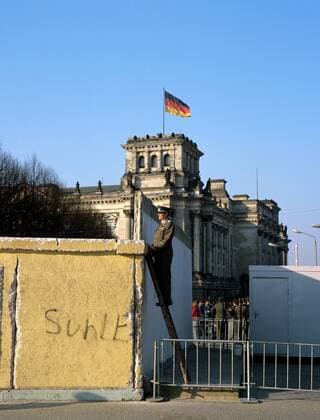 Volkspolizist steht auf einer Leiter und schaut über die Berliner Mauer am Reichstag