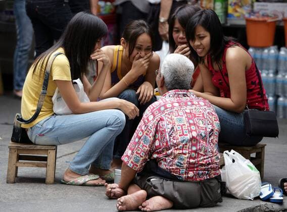 Bangkok - Geschichtenerzähler auf einem Markt unterhält junge Mädchen