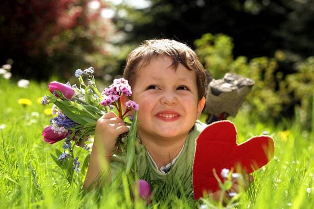 Junge mit gepflückten Blumen und Herz als Geschenk zum Muttertag